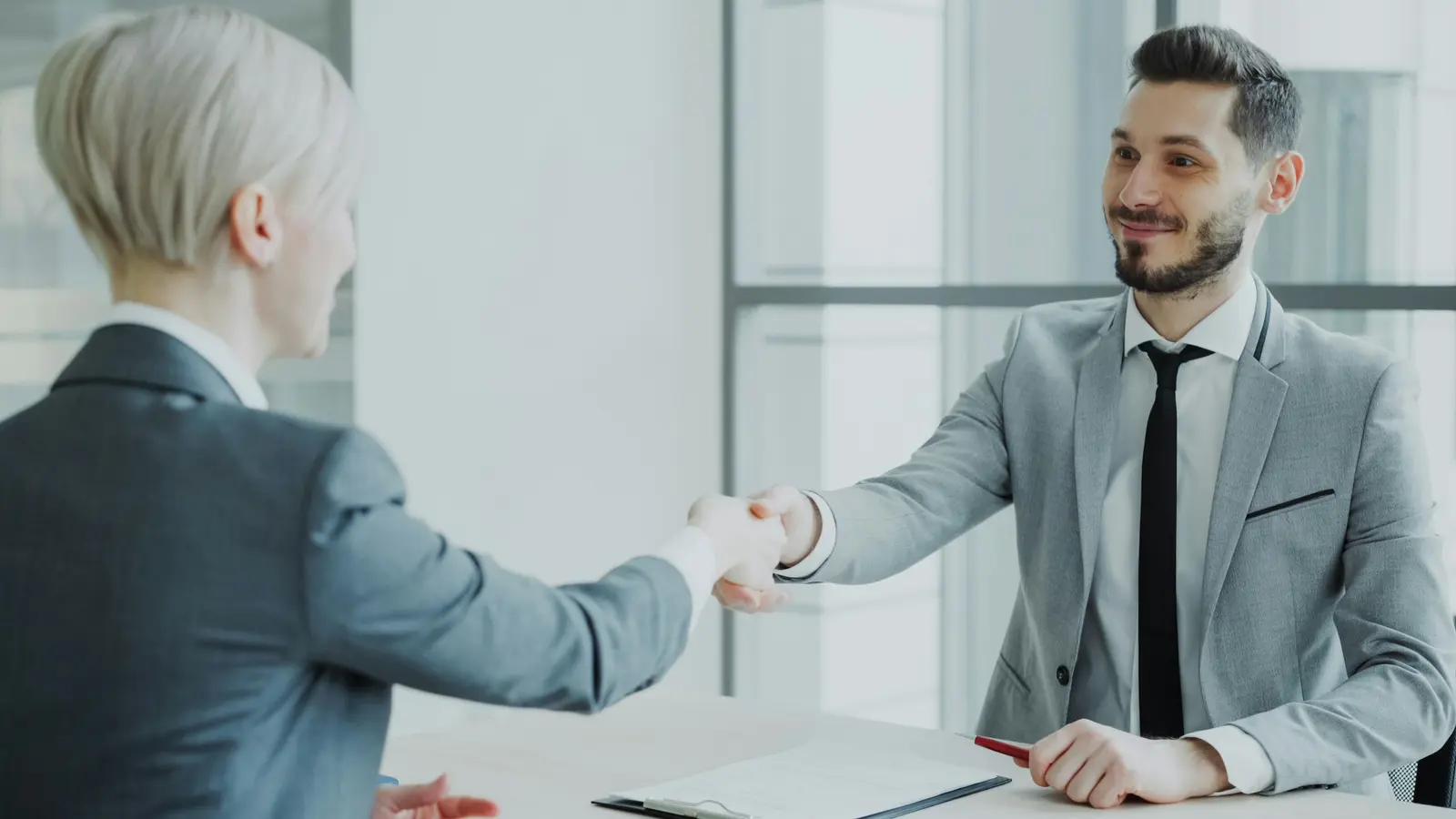 Two professionals shaking hands across a desk in a bright office