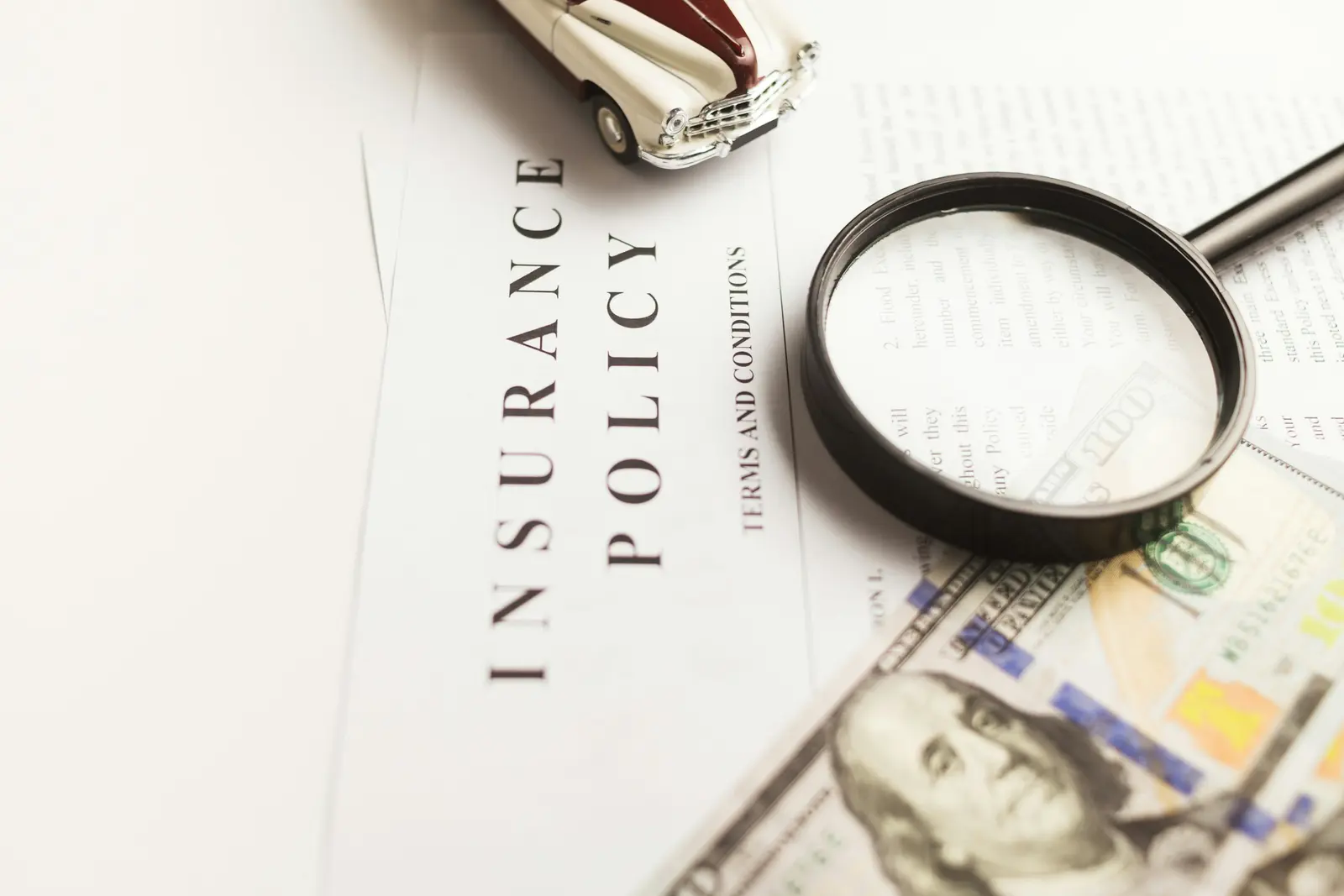 Insurance policy document under a magnifying glass beside banknotes
